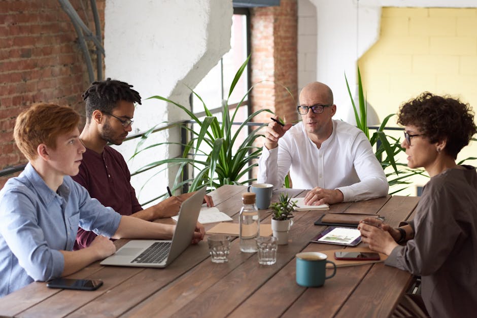 Business professionals collaborating in a modern office with laptops and plants on a wooden table.