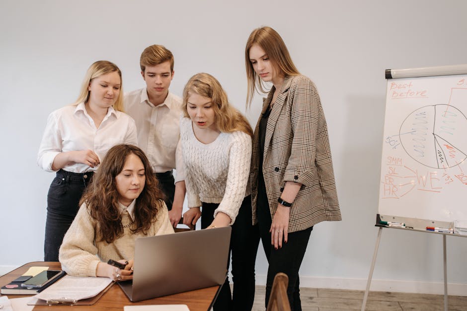 Group of young adults collaborating on a project with a laptop and whiteboard in a modern office setting.